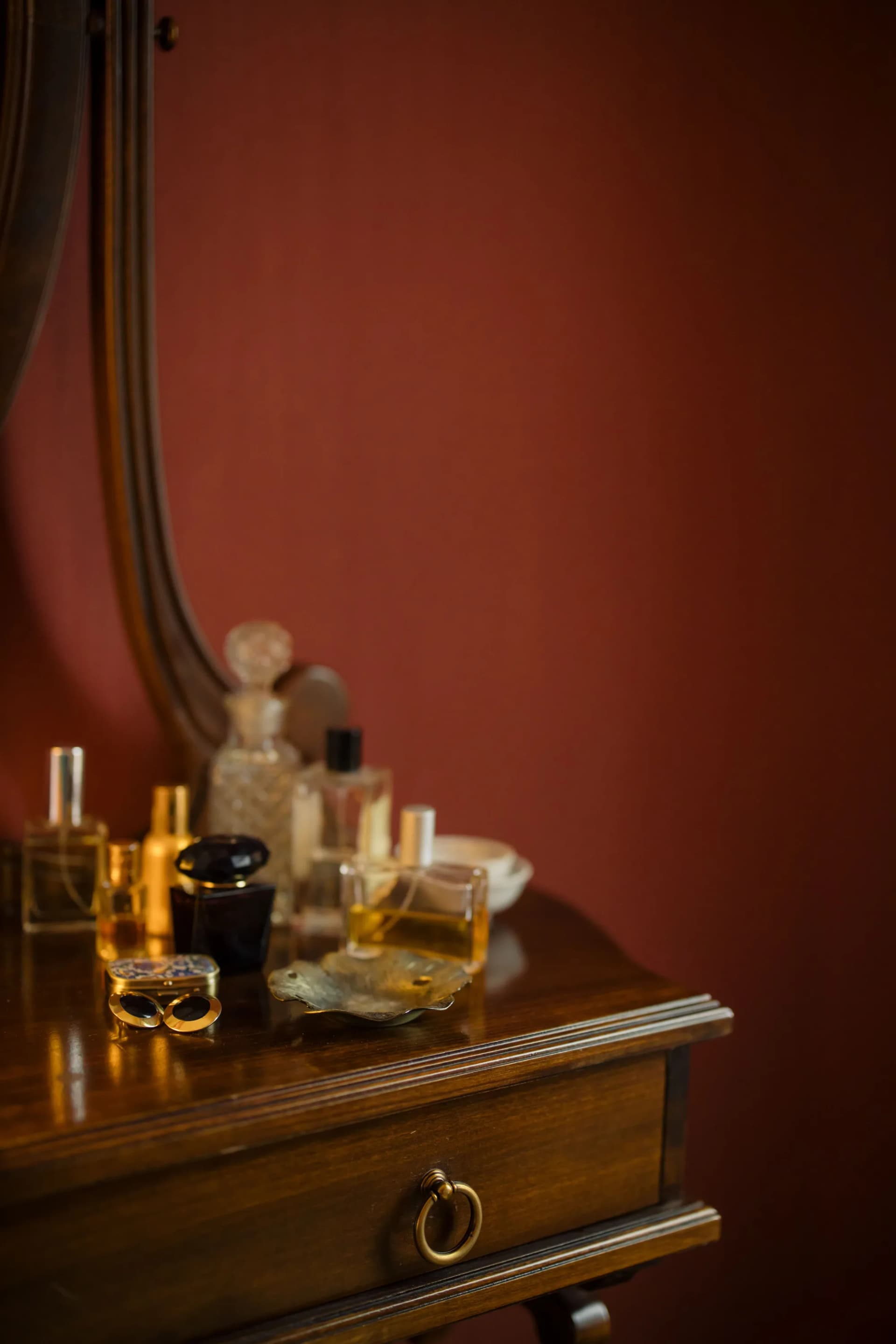 Vintage perfume bottles and a trinket dish arranged on a wooden dresser beneath a mirror